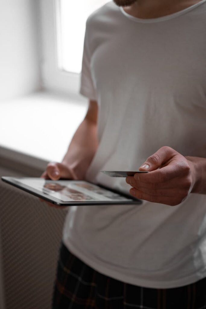 Person holding tablet and credit card indoors, symbolizing cashless and modern transactions.